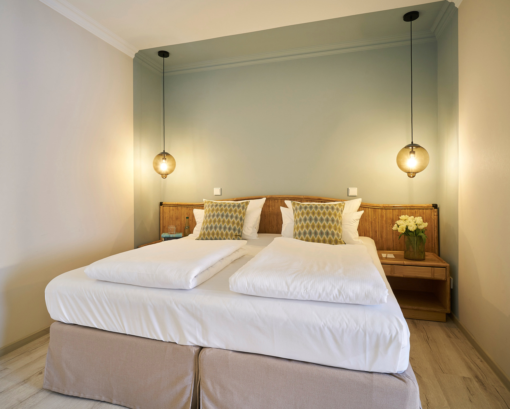 Sage green room — rattan headboard, amber pendants