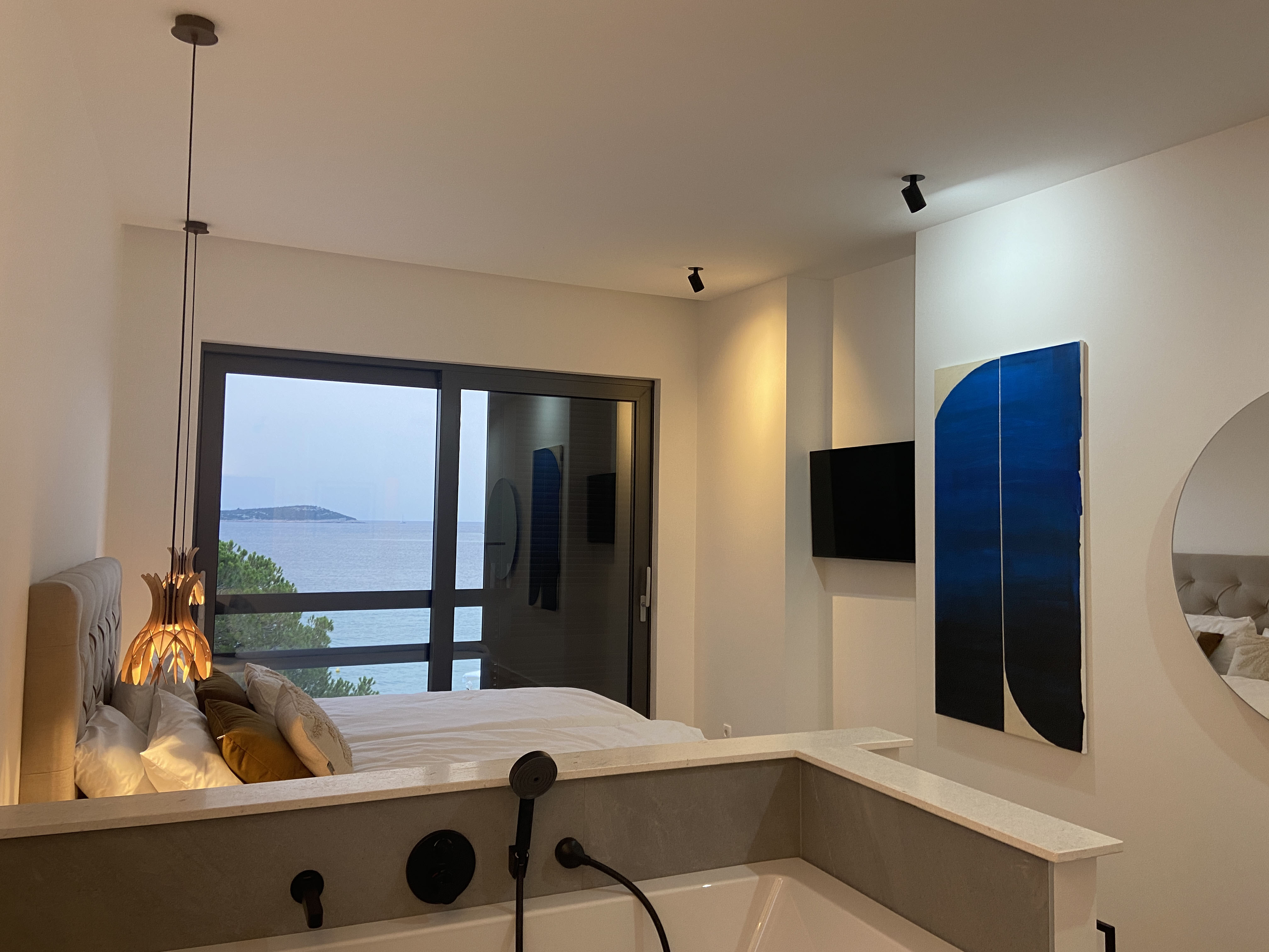 Master bedroom — blue diptych artwork, sea view, freestanding bath
